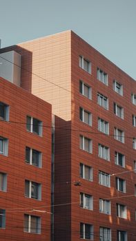 A contemporary red brick building with numerous windows in an urban environment captured during daylight.