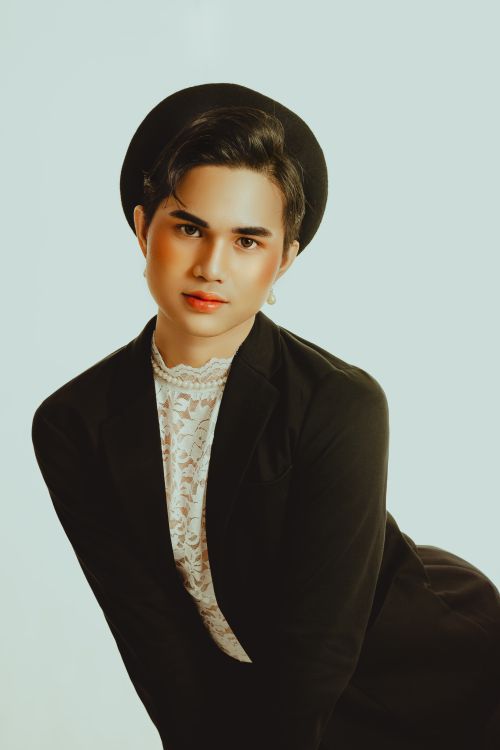 Free Stylish studio portrait featuring a person in a black suit and hat posed against a soft white background. Stock Photo