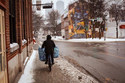 A person on a bicycle carrying bags rides through snow-covered city streets in Québec.