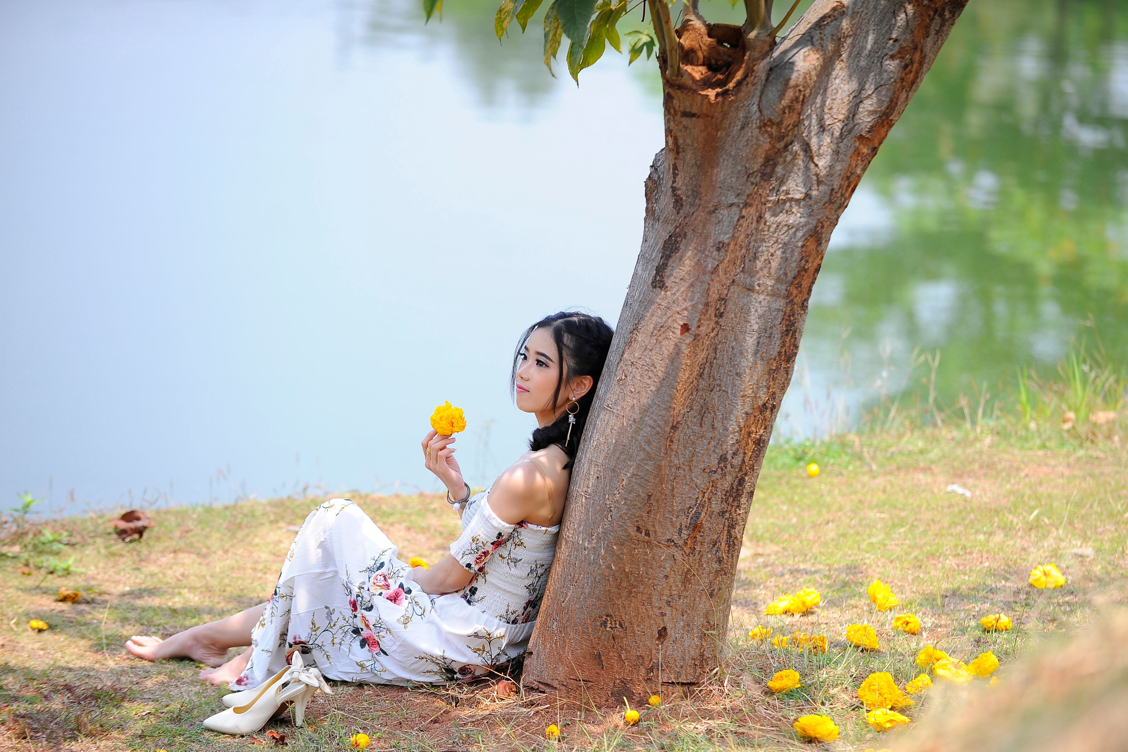 A serene scene of a woman in a floral dress by the lakeside under a summer tree.
