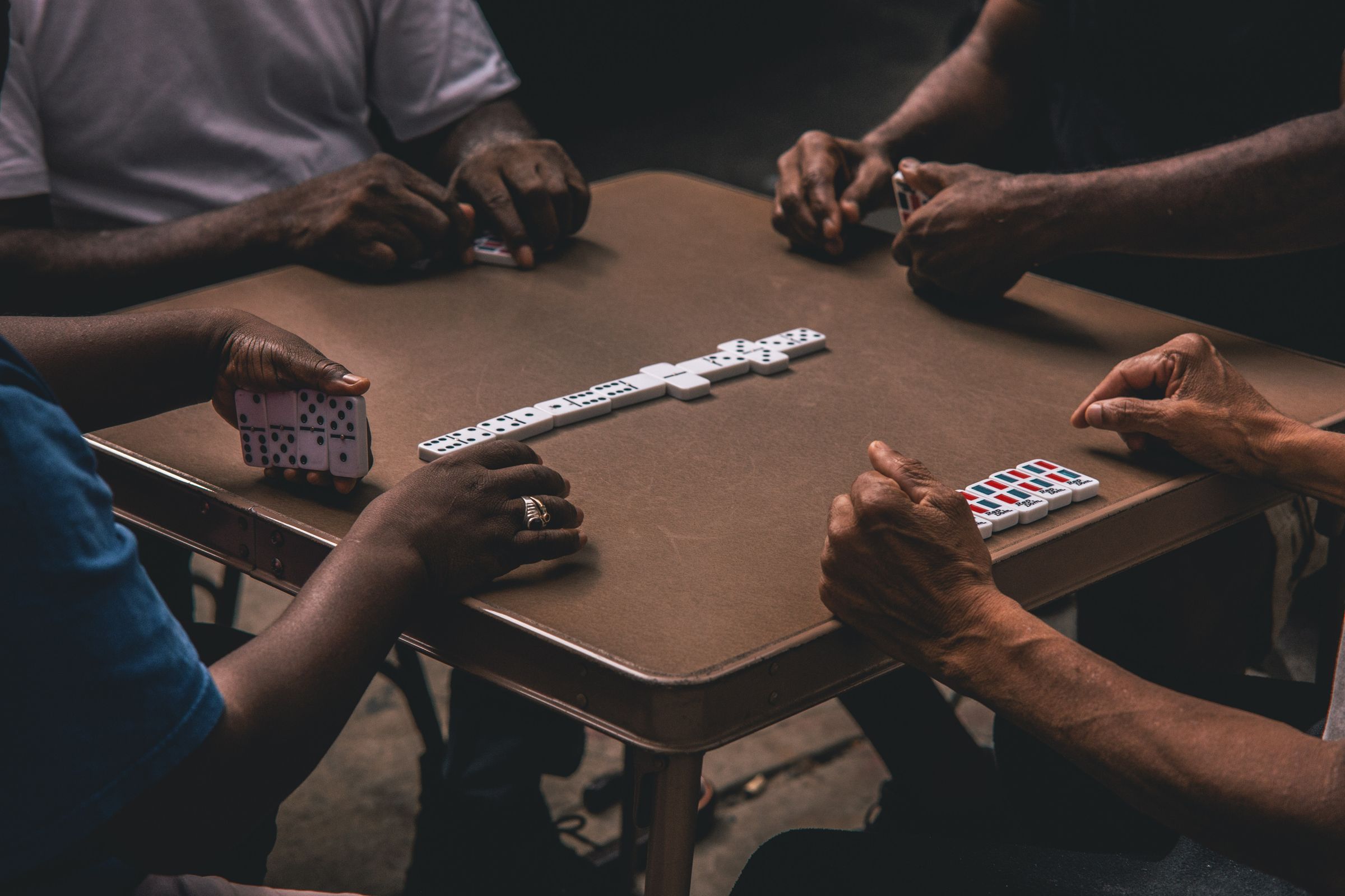 Four people gathered around a table playing dominoes