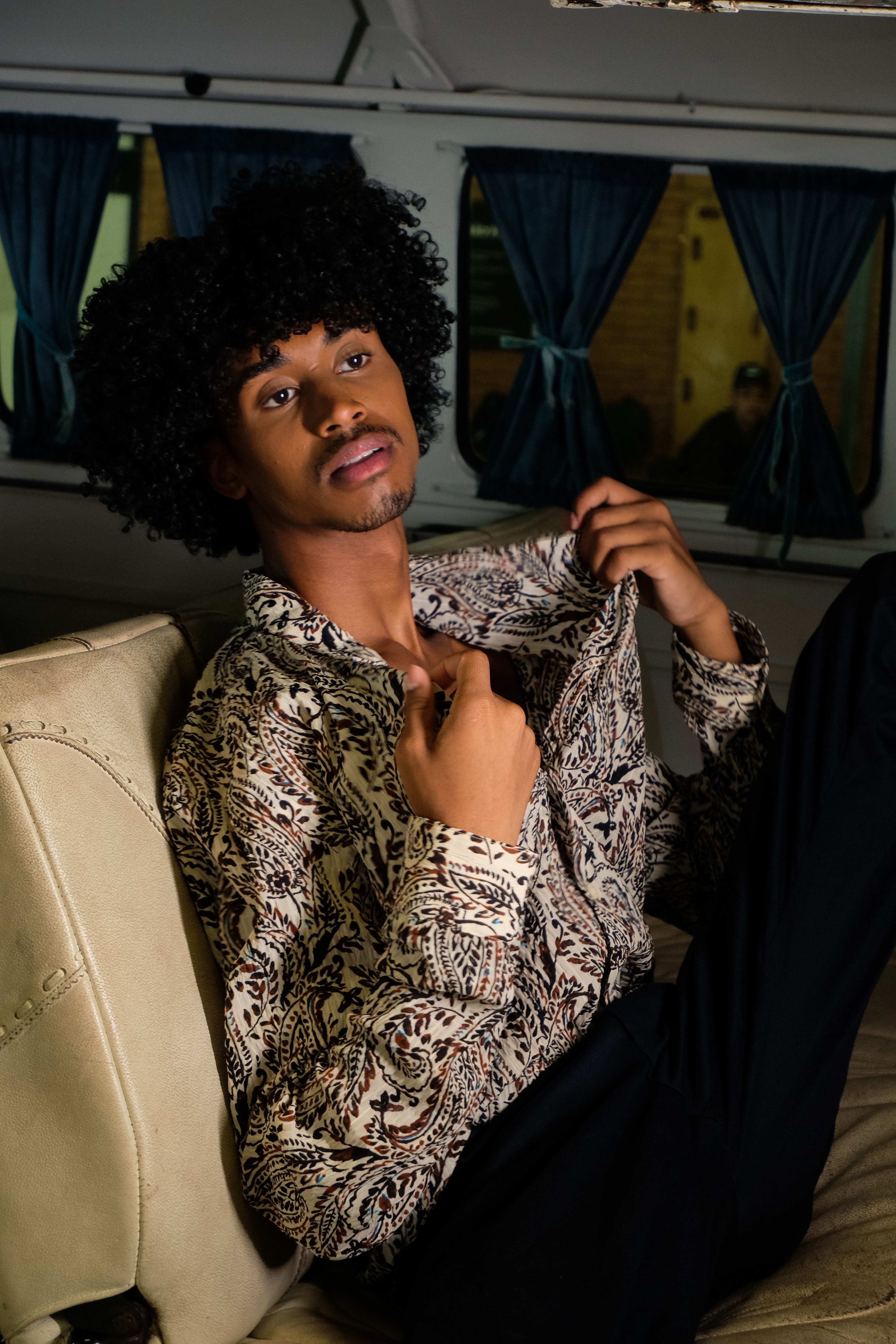 Portrait of a fashionable man with curly hair posing in a vintage van in São Paulo.