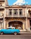 一辆经典的蓝色古董车驶过哈瓦那一座历史悠久的殖民建筑