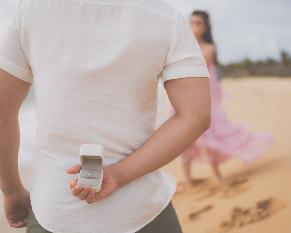 A man hiding an engagement ring behind his back on a beach