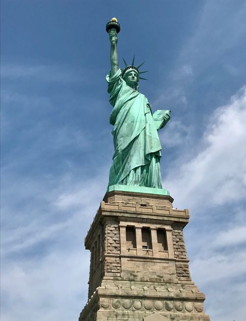 Free Iconic Statue of Liberty standing tall against a vibrant blue sky in New York City. Stock Photo