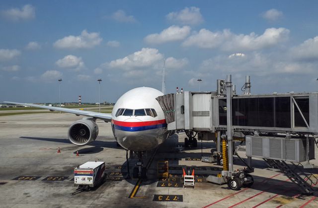 A commercial airplane parked at Kuala Lumpur airport, connected to a passenger boarding bridge under a clear blue sky. — arriving in Kuala Lumpur
