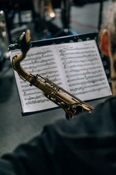 Close-up of a saxophone with a sheet music stand in a dimly lit setting.