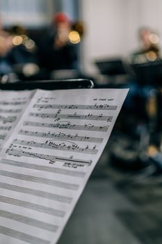 Detailed view of a music sheet with blurred musicians rehearsing in the background.