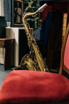 Close-up of a saxophone placed beside a red chair in a warmly lit indoor setting.