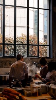 Professional chefs work together preparing meals in a restaurant kitchen with steam rising.