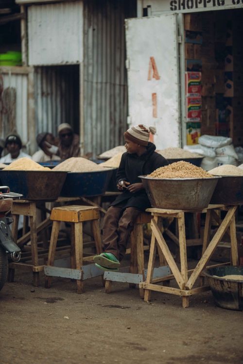 Free A boy sits among bowls of grains in an outdoor market, providing a glimpse into daily life. Stock Photo