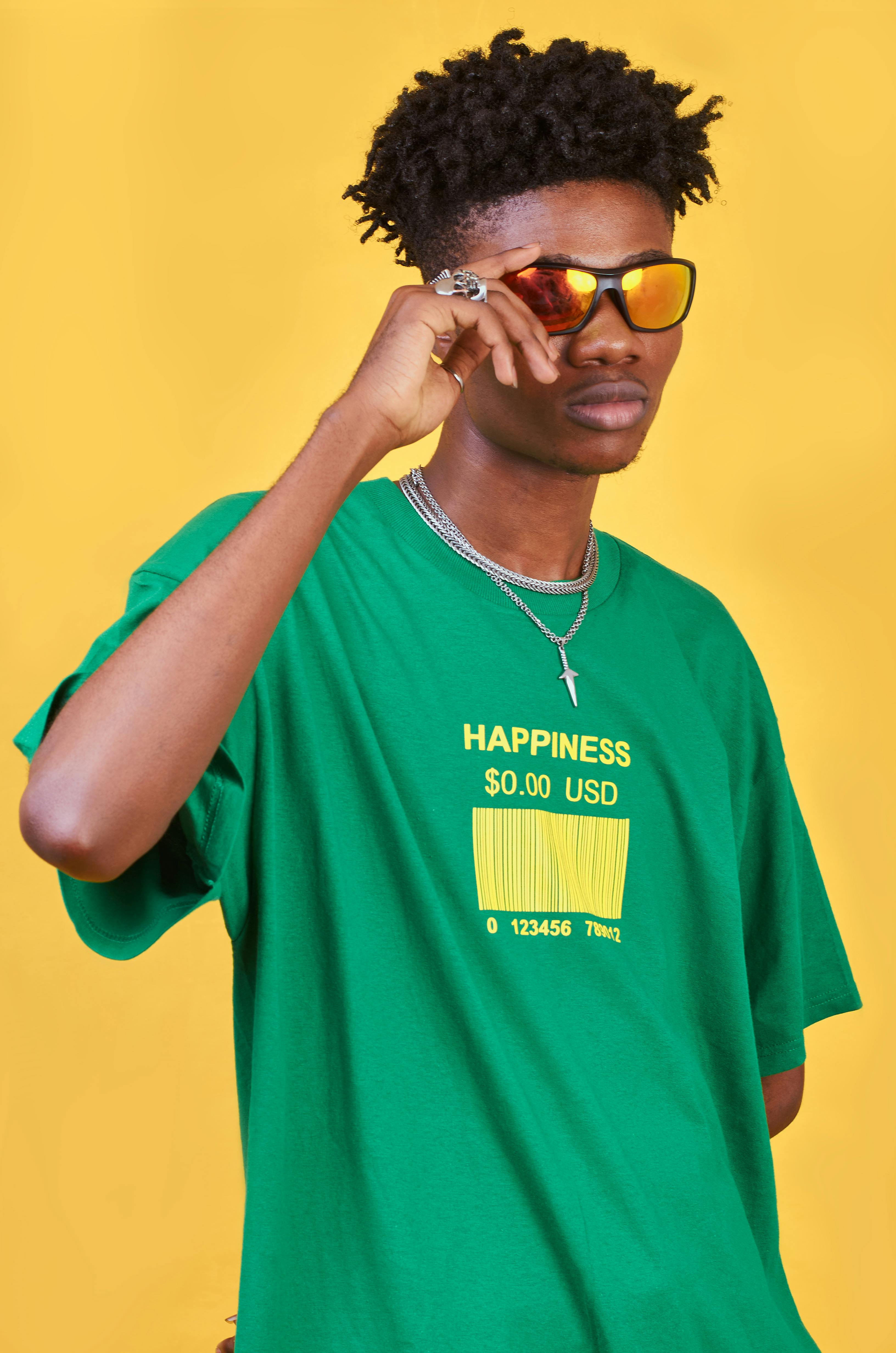 Young man with dreadlocks and sunglasses wearing a green t-shirt on a yellow background.