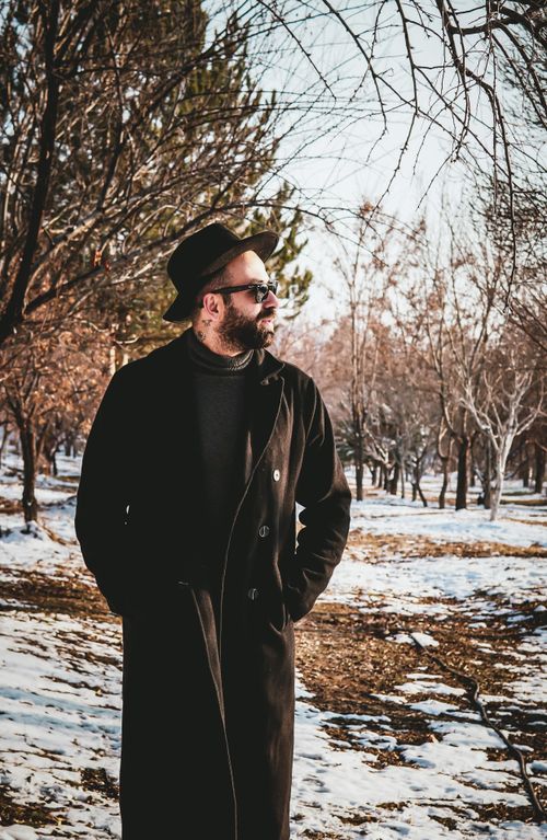 Free A fashionable bearded man in winter attire strolling through a snowy park on a sunny day. Stock Photo