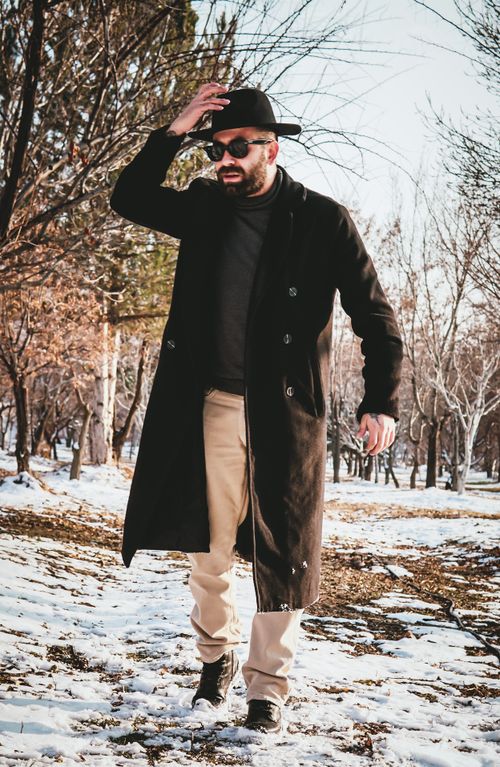Free A bearded man in a coat and hat walking through a snowy park on a winter day. Stock Photo