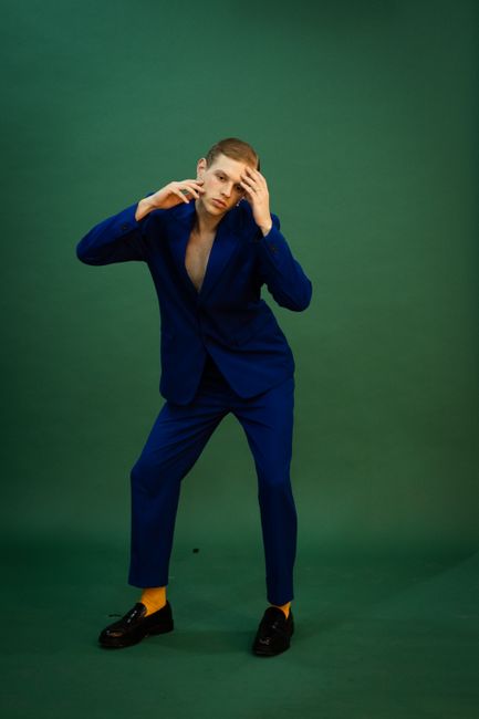 Fashionable man striking a pose in a navy blue suit against a green background during a studio shoot.