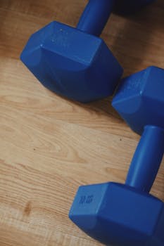 Close-up photo of blue dumbbells resting on a wooden floor, perfect for fitness themes.