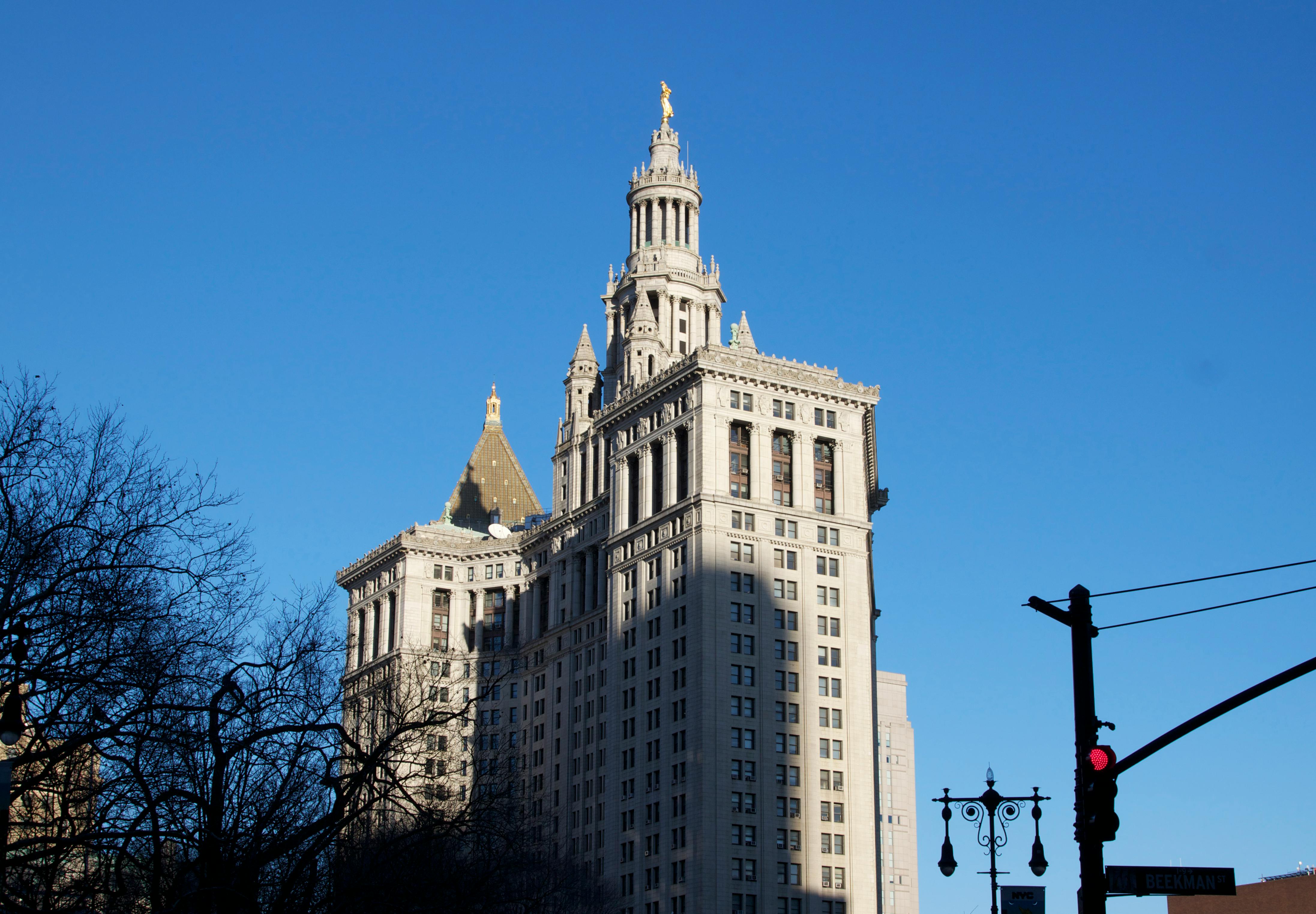 The iconic New York Municipal Building stands tall against a clear blue sky, surrounded by city elements.