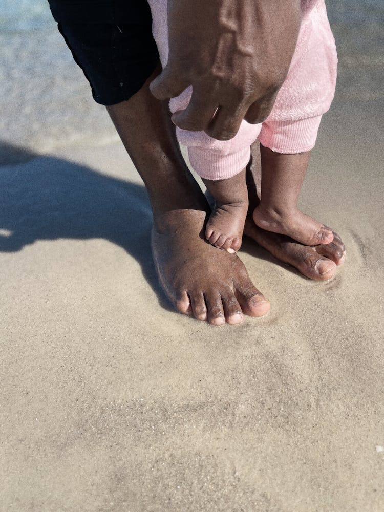 Parent And A Baby Standing Barefoot On Shore