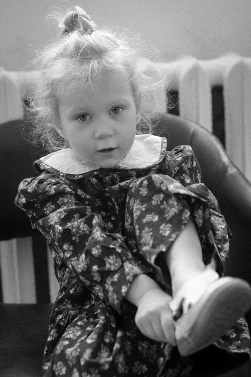 Free Charming black and white portrait of a little girl in a floral dress sitting indoors. Stock Photo