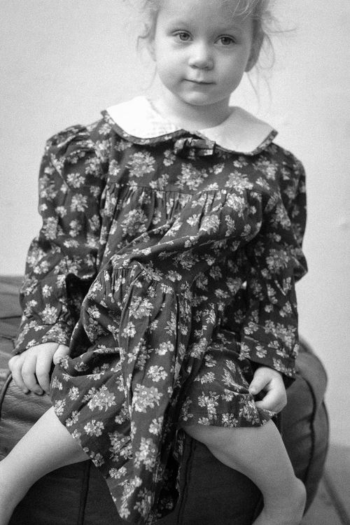 Free Charming black and white portrait of a young girl in a vintage floral dress sitting indoors. Stock Photo