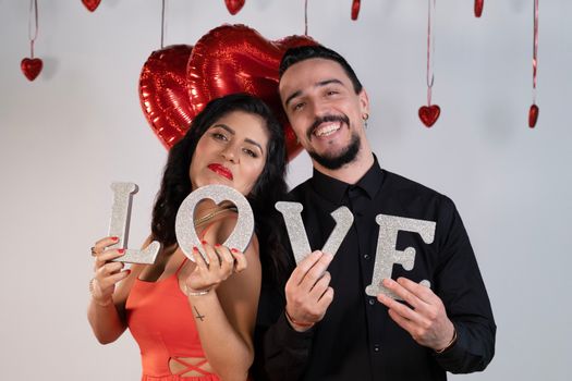 Joyful couple holding a glittery 'LOVE' sign, perfect for Valentine's Day expressions.