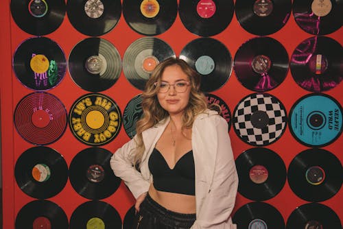 Blonde Woman in White Shirt Posing Against Vinyl Records on Wall