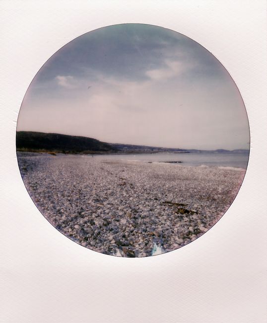 A tranquil pebble beach scene with expansive sky and distant horizon.