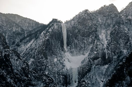 Breathtaking view of snow-covered mountains with a cascading waterfall in grayscale.