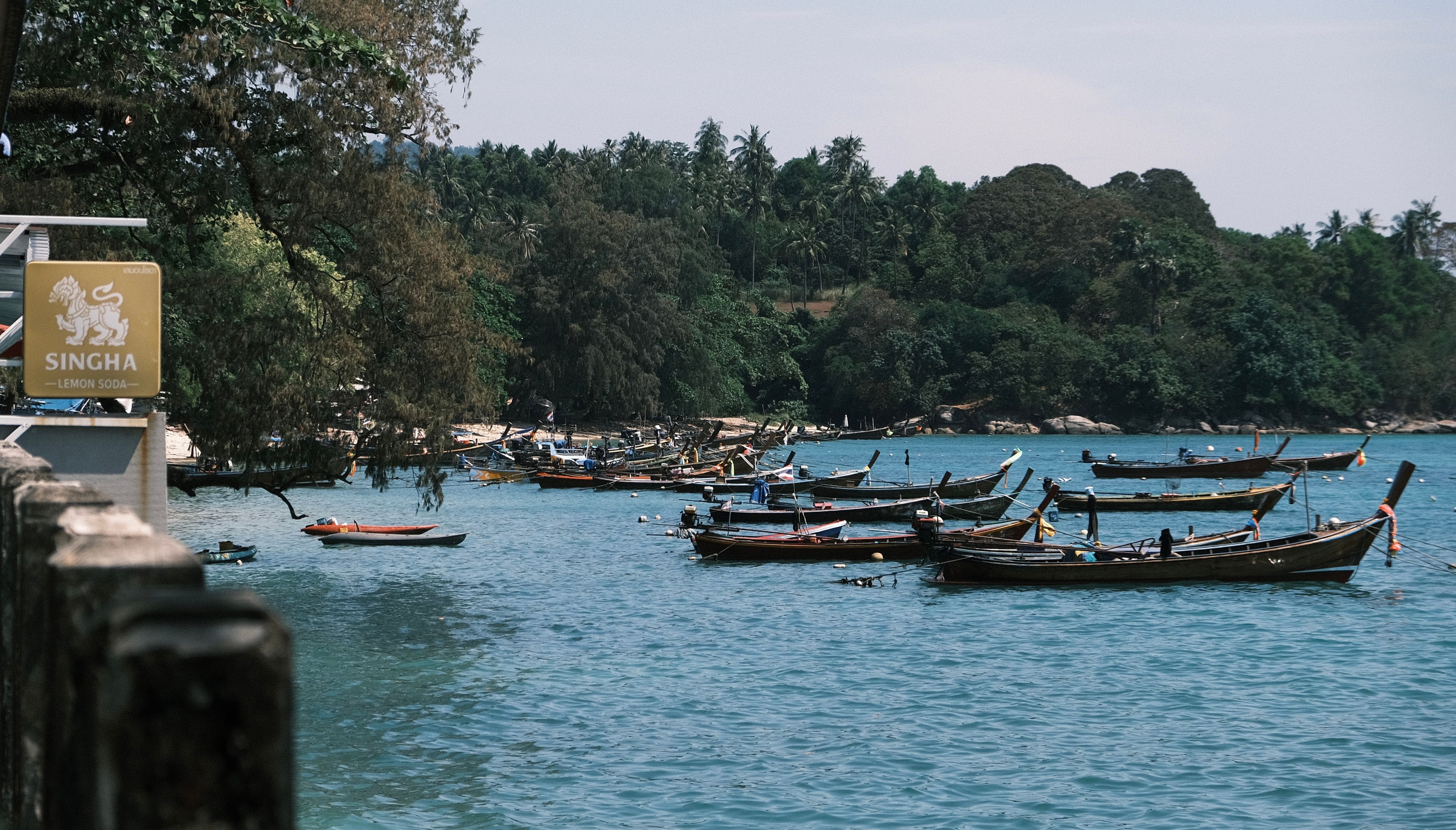 Longtail boats float on a tranquil tropical lake surrounded by lush green forest.