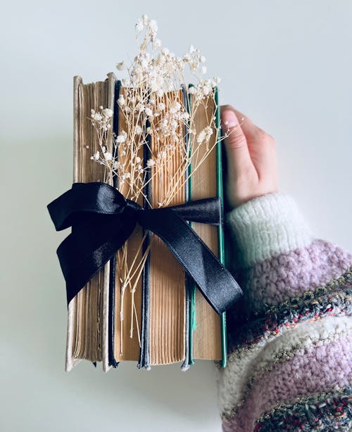 Hand Holding Bundle of Books and Flowers