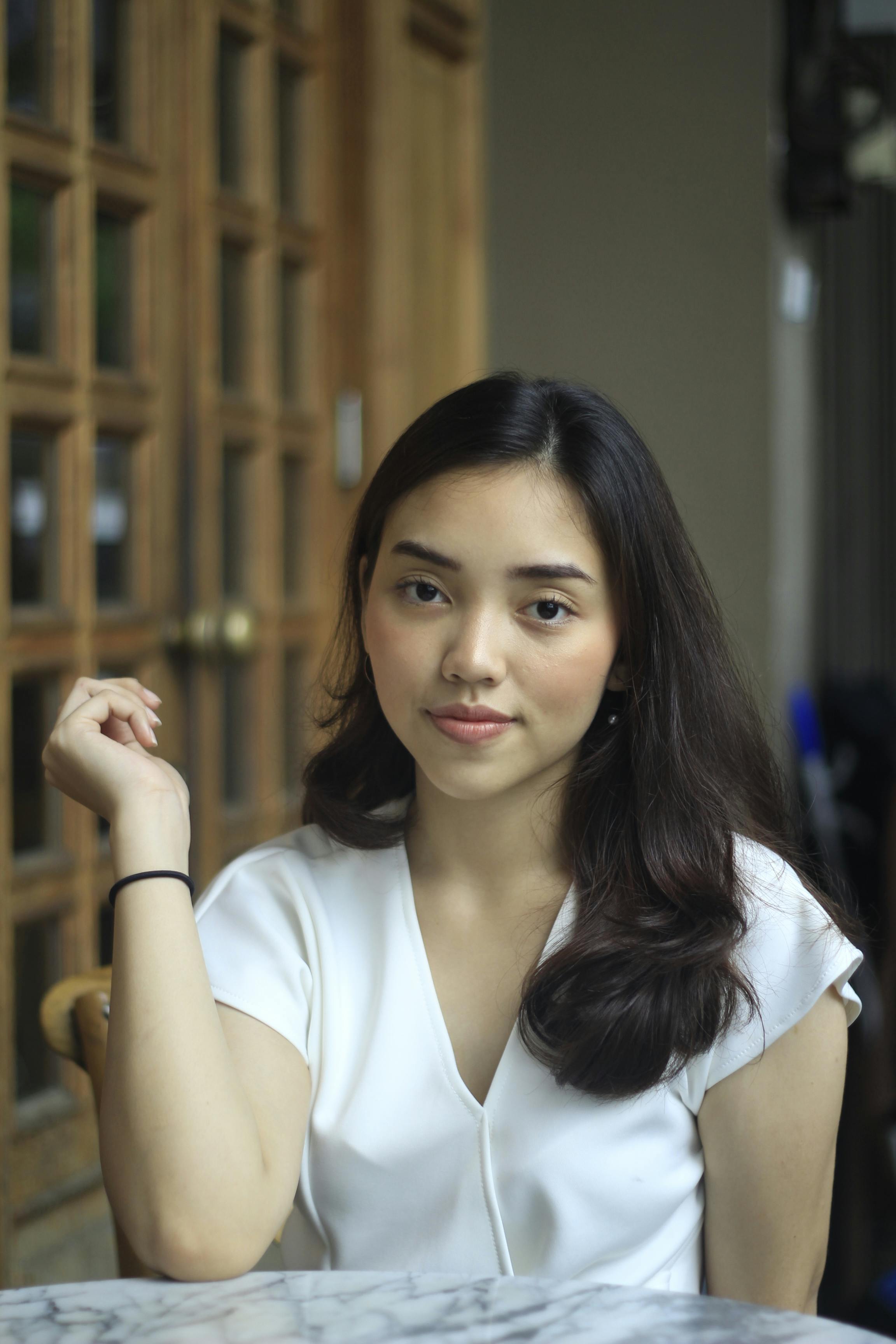 A young woman sitting at a table with her hands on her lap · Free Stock  Photo