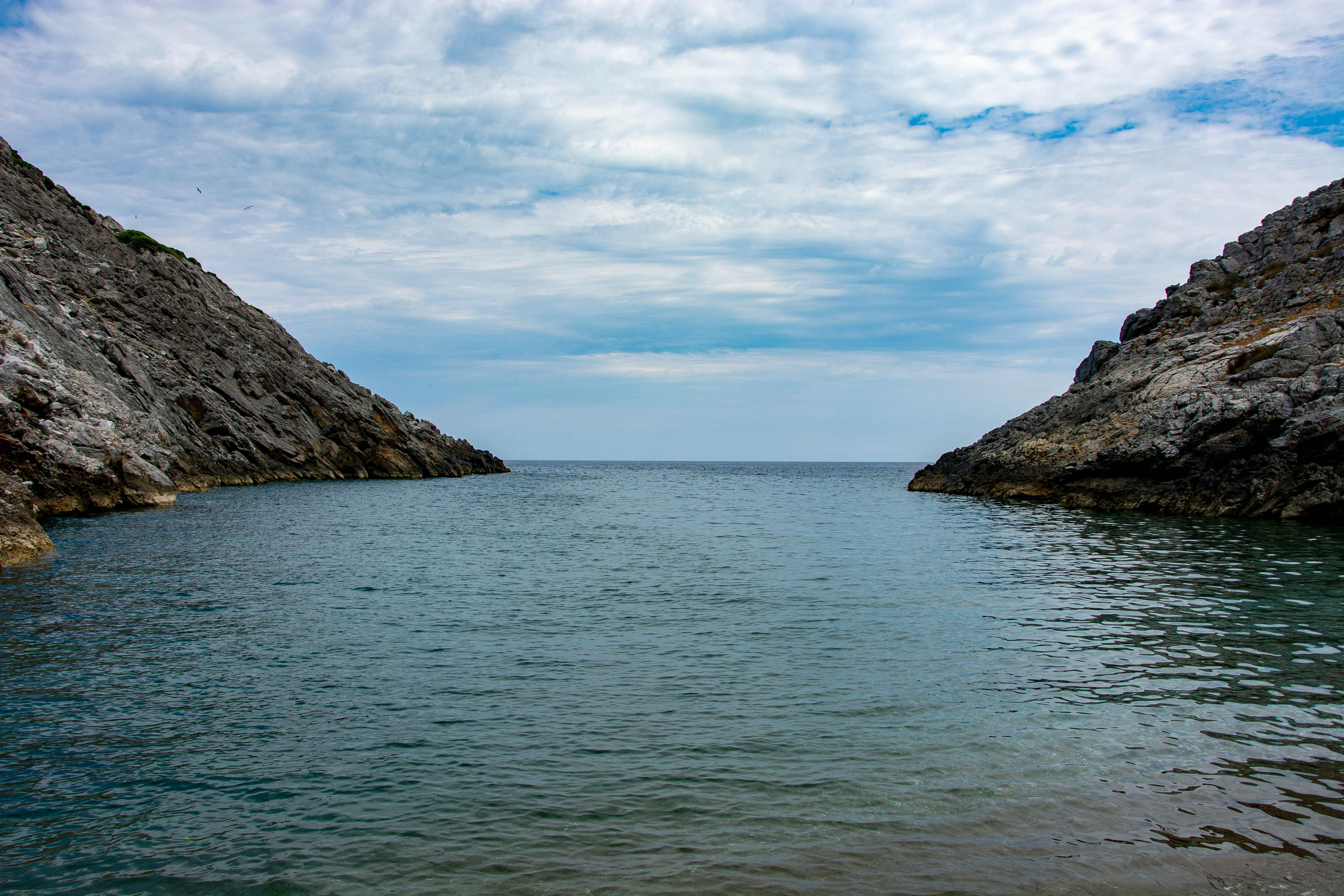 Tranquil ocean view between rocky cliffs under a lightly clouded sky.