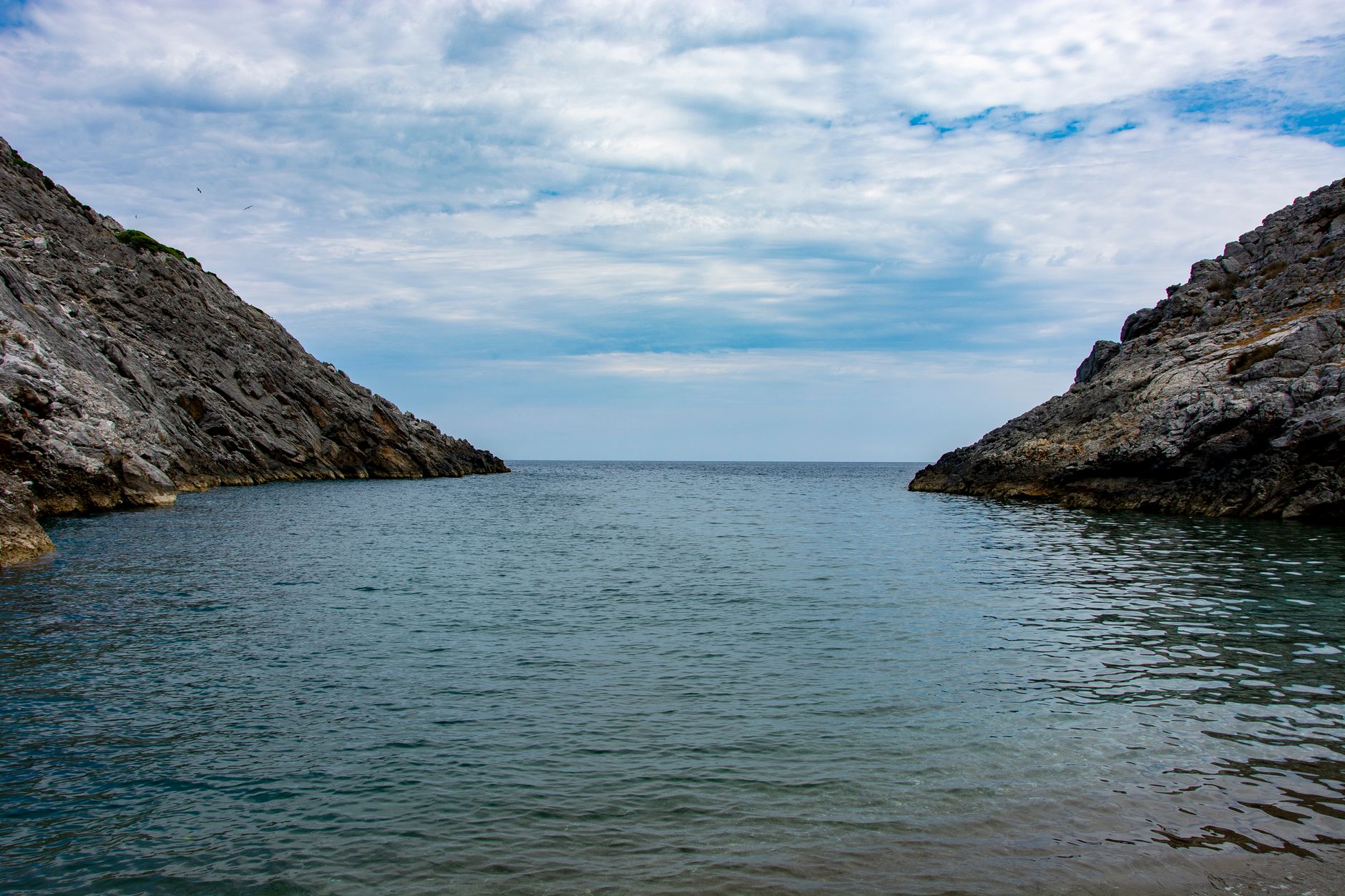 Tranquil ocean view between rocky cliffs under a lightly clouded sky.