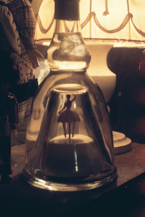 Free A vintage ballerina figurine encased in a glass bottle, illuminated by warm lamp light creating a nostalgic atmosphere. Stock Photo