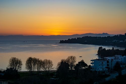 Free A tranquil sunset over a calm sea with distant mountains and coastal town. Stock Photo