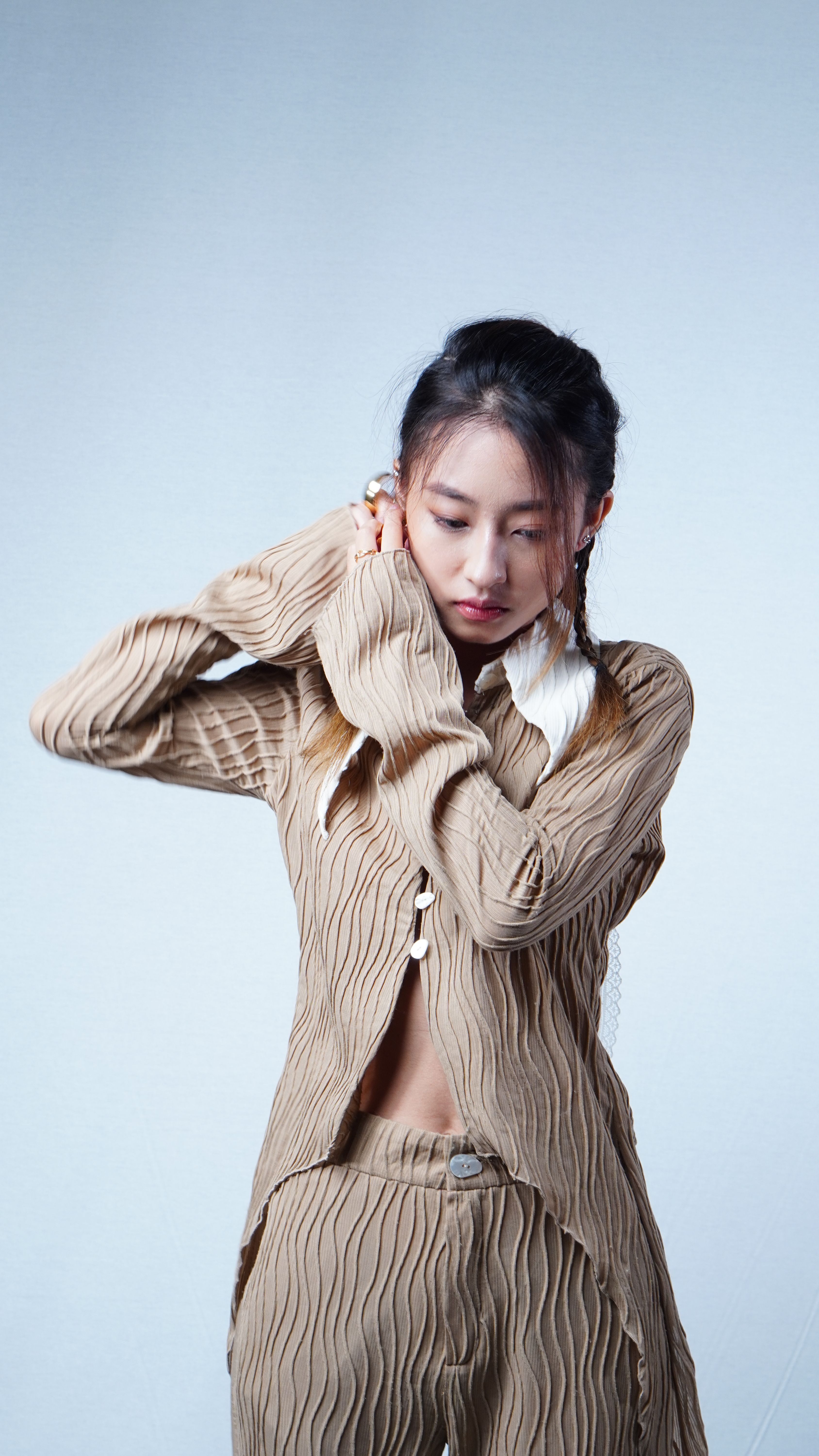 Fashion portrait of a woman looking down, wearing beige textured clothing against a white background.