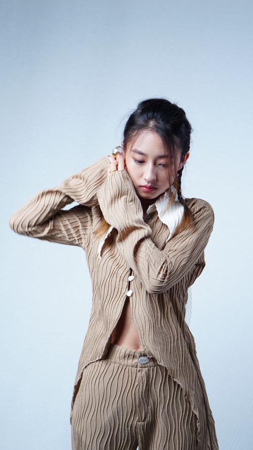 Free Fashion portrait of a woman looking down, wearing beige textured clothing against a white background. Stock Photo