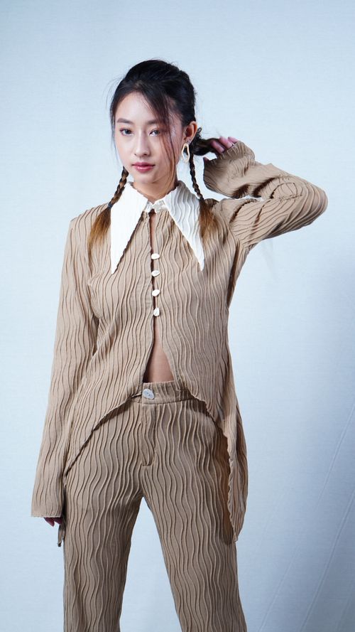 Free Young woman posing in a beige textured outfit with a confident expression on a white background. Stock Photo