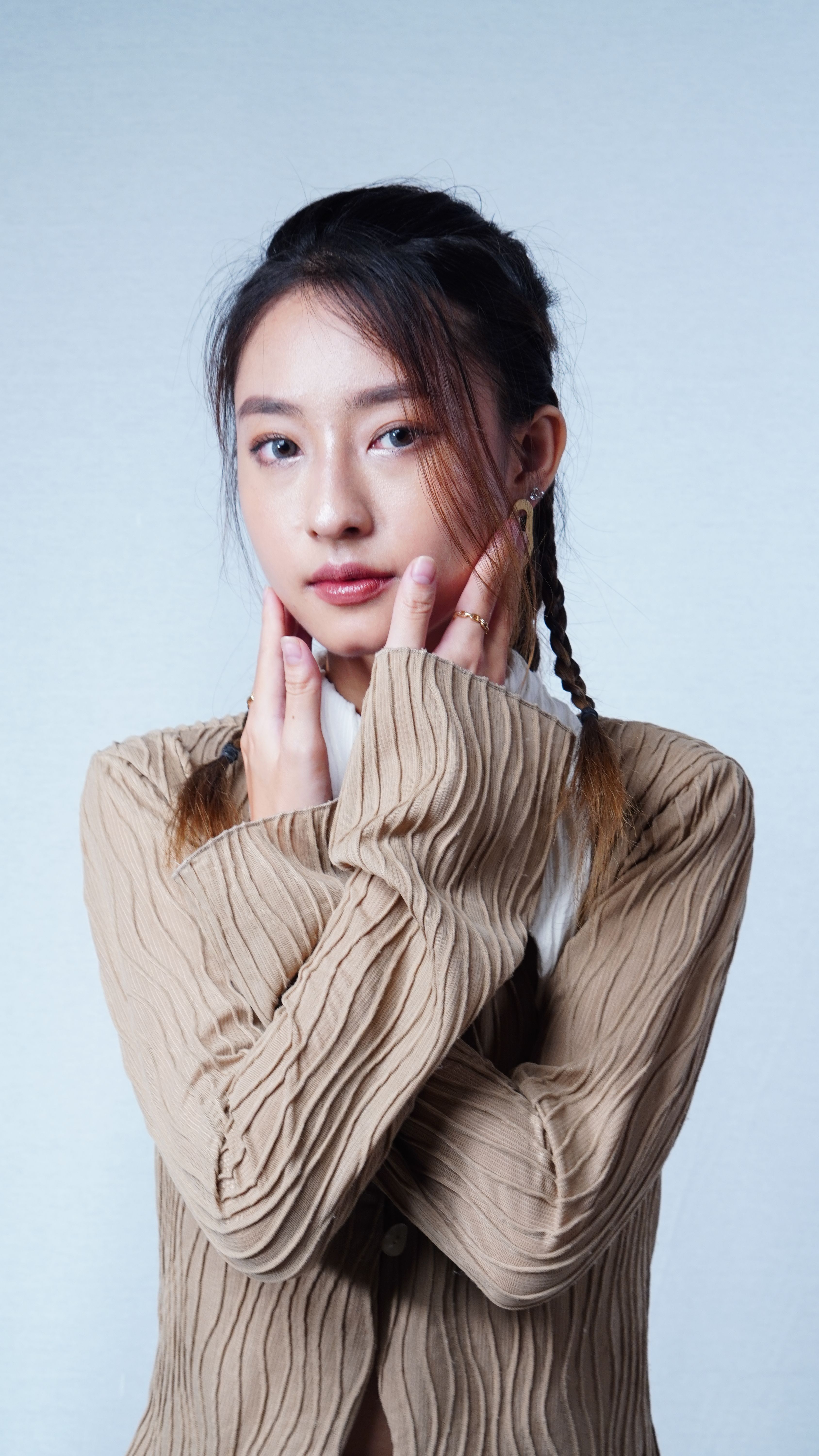Elegant portrait of a young woman with braided hair wearing a beige top, offering a serene expression.