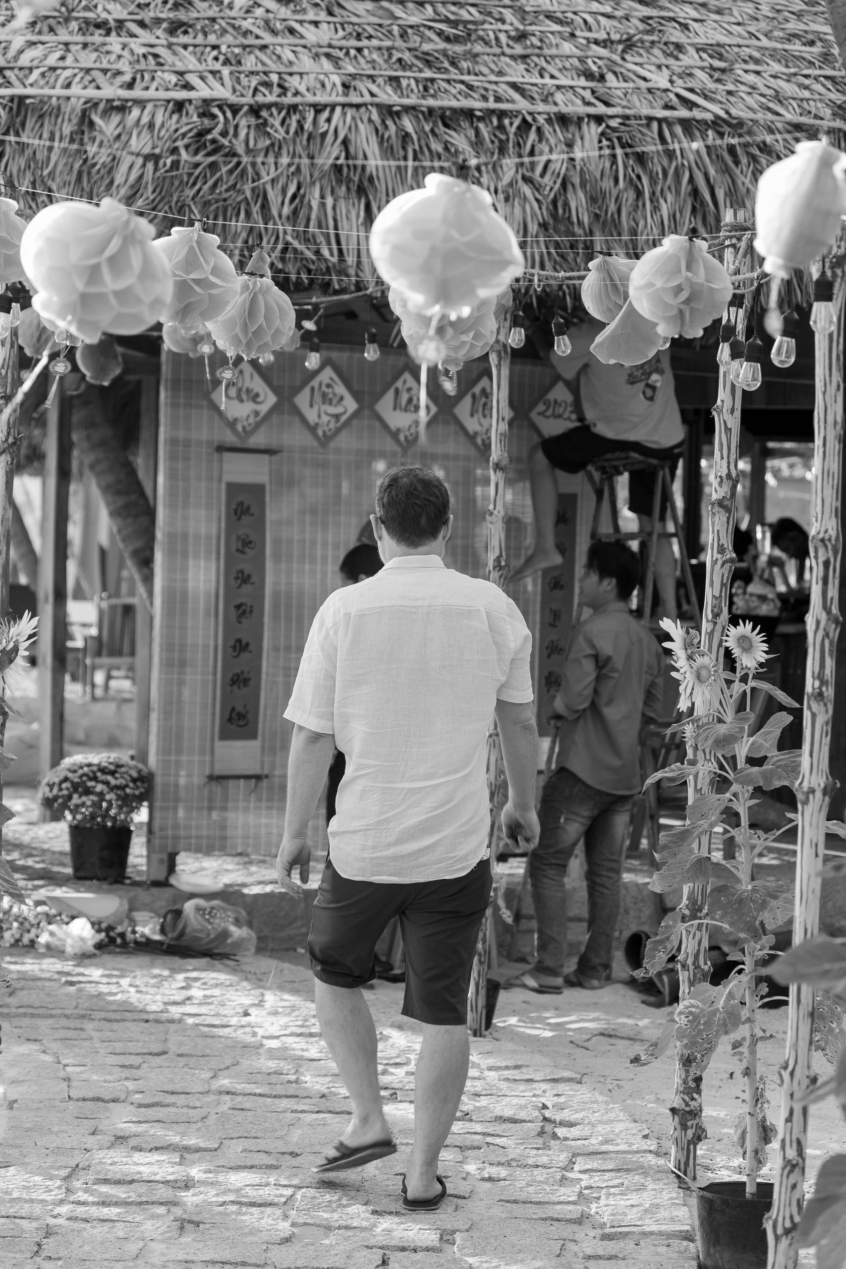 A man walks down a cobblestone street in a traditional market setting, captured in black and white.