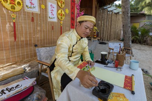 Free Asian man creating traditional calligraphy art at a decorated table outdoors. Stock Photo