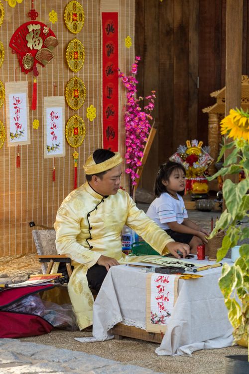 Free Man in traditional clothing writes calligraphy at cultural festival table with child nearby. Stock Photo