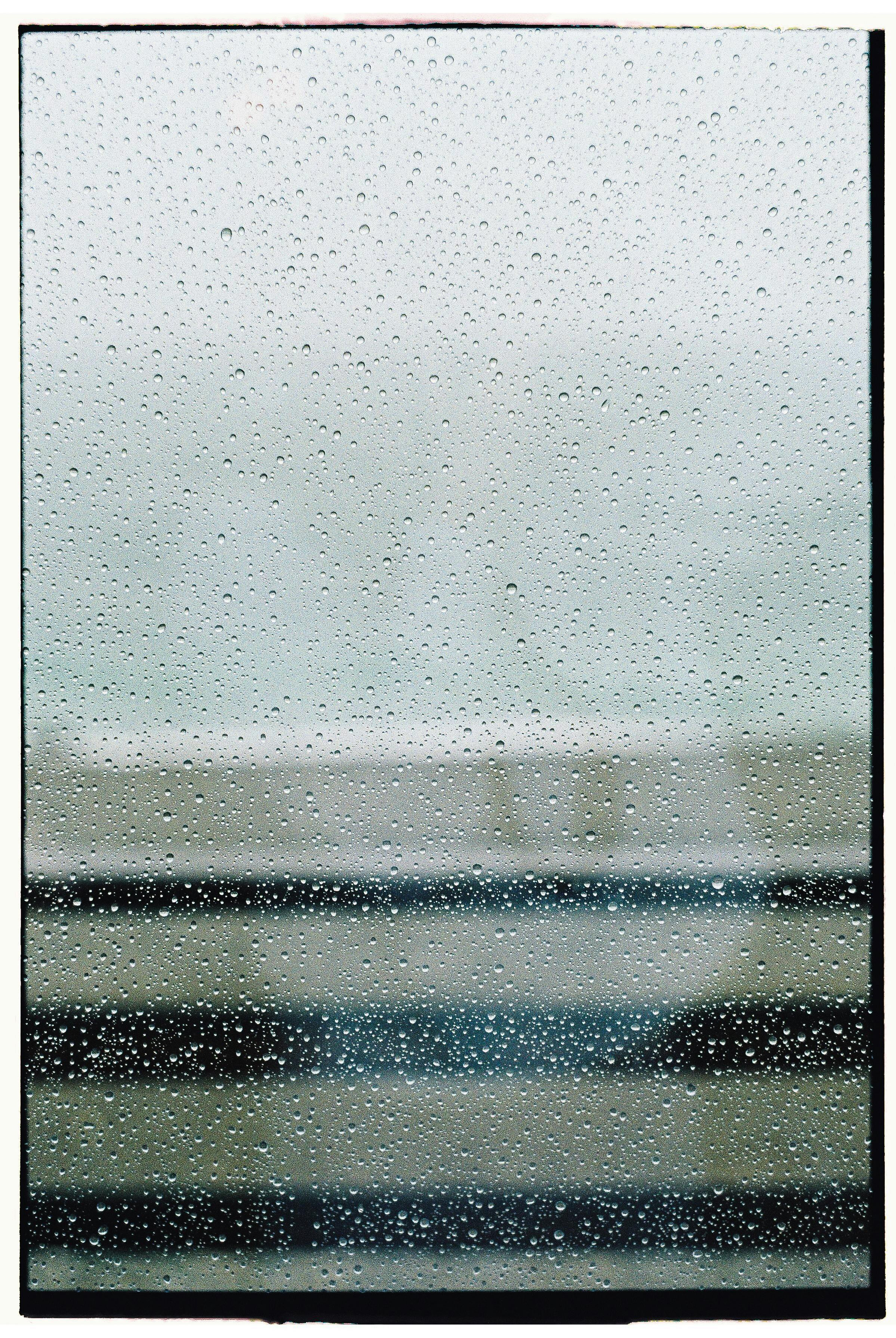 Close-up of raindrops on a window with blurred horizontal lines in the background.