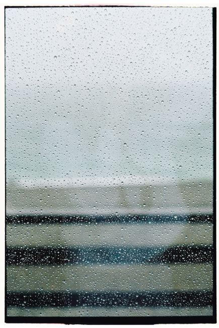 Close-up of raindrops on a window with blurred horizontal lines in the background.