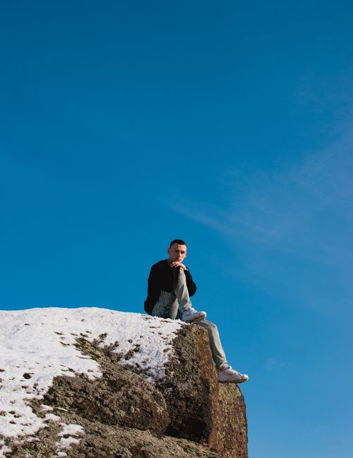 Free A man sits alone on a snowy cliff edge under a clear blue sky, capturing a moment of solitude and reflection. Stock Photo