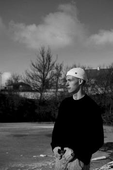 Young man in winter attire standing in rural setting. Black and white portrait capturing cold atmosphere.