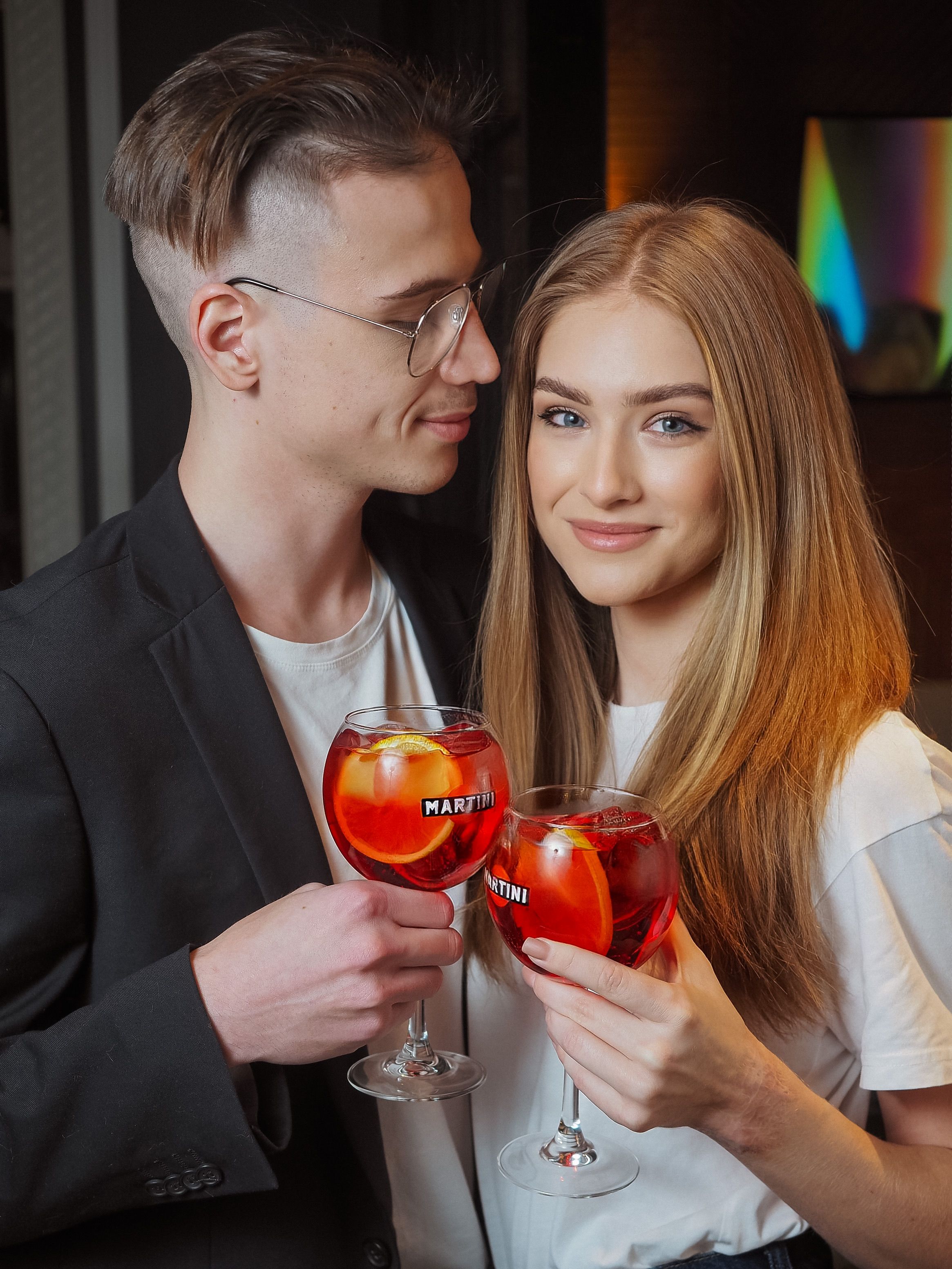 Smiling young couple enjoying cocktails in a relaxed indoor setting.