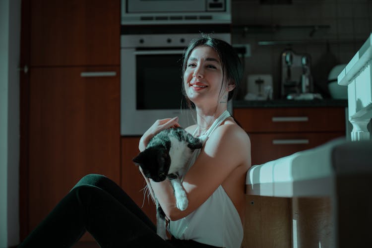 Smiling Woman With A Cat In Her Arms Sitting On The Kitchen Floor