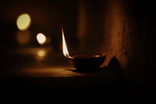 Free A single diya illuminating a dark room with its warm, flickering flame for a serene atmosphere. Stock Photo