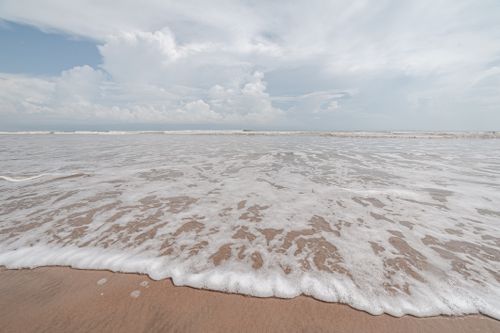Free Gentle waves lapping at a sandy beach under a vast cloudy sky. Stock Photo